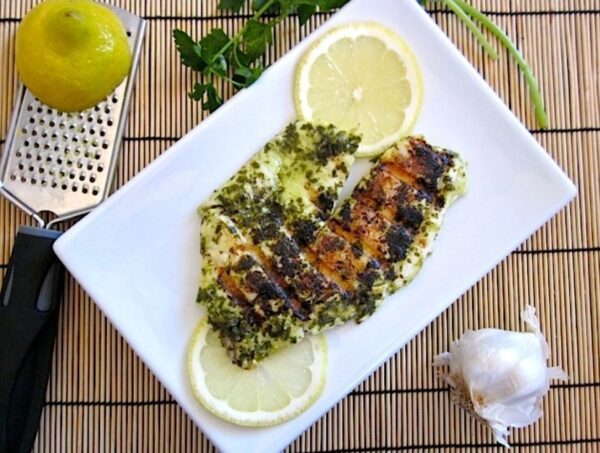 Fish dressed with Seafood rub on a plate garnished with lemon.